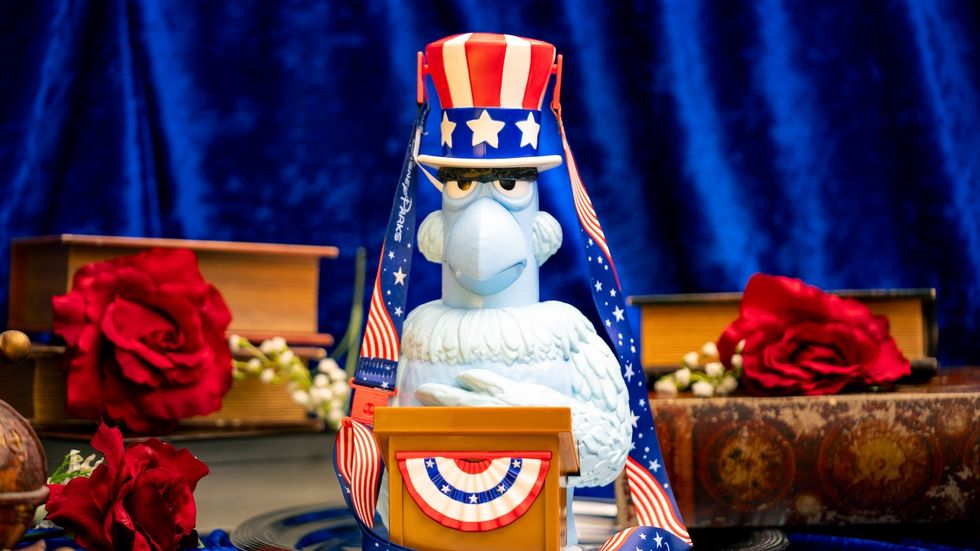 Patriotic Sam Eagle popcorn bucket with stars and stripes hat, surrounded by red roses and antique books.