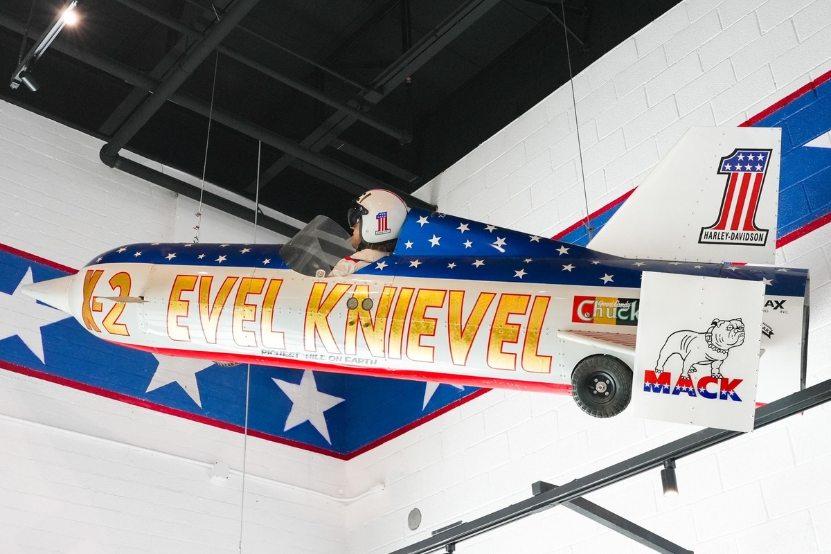 Patriotic-themed rocket bike display with "Evel Knievel" text, suspended indoors.