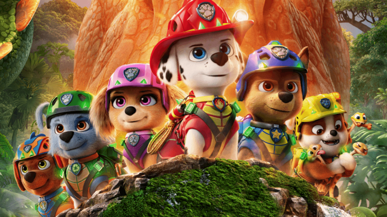 Paw Patrol pups in colorful gear explore a jungle, standing in front of a large dinosaur figure.