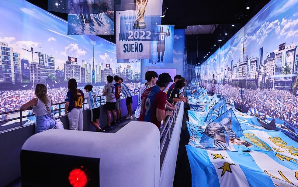 People admire soccer-themed exhibits with large Argentina flags and projected crowds.