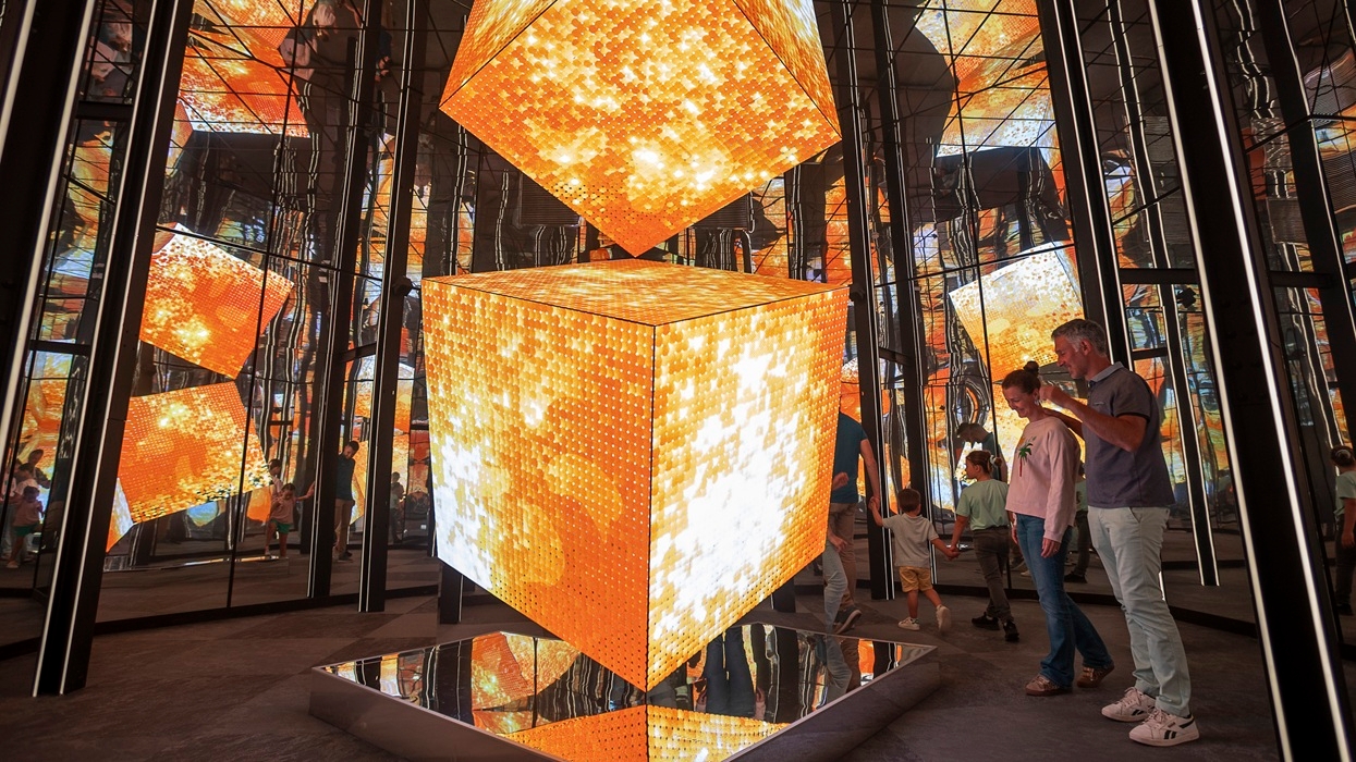 People admiring glowing cubes in a mirrored room with orange and white patterns, at Pulse! The Electric Odyssey