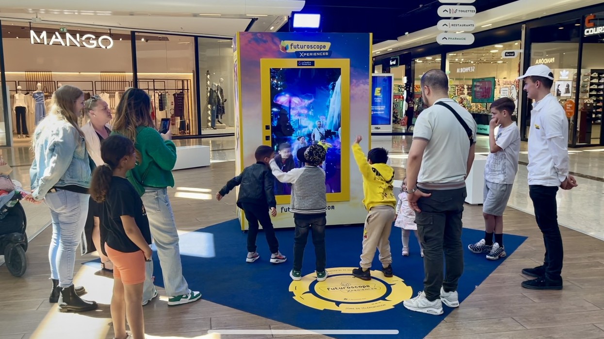 People and children interact with a large digital display at a shopping mall exhibit.