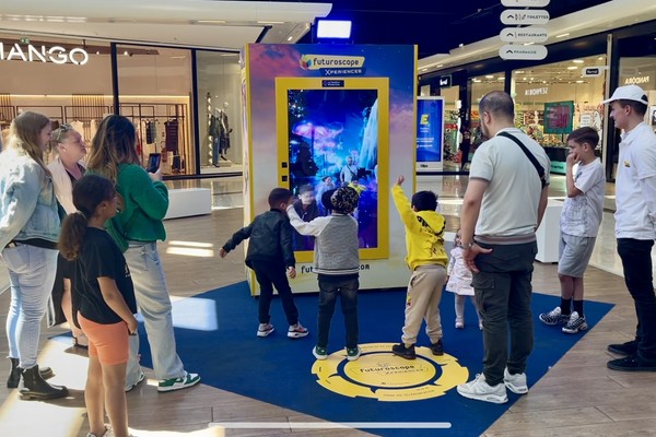 People and children interact with a large digital display at a shopping mall exhibit.