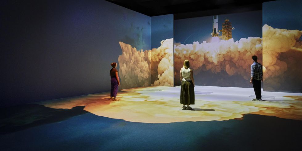 People at Our Story with David Attenborough with a rocket launch projection on the walls and floor.