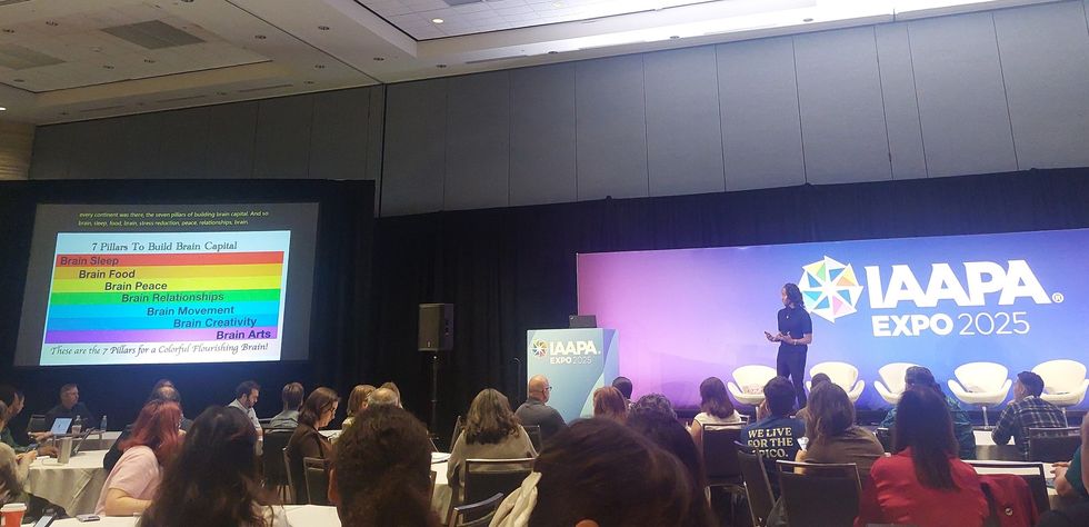 People attending a presentation at IAAPA Expo 2025 with slides on brain capital pillars.