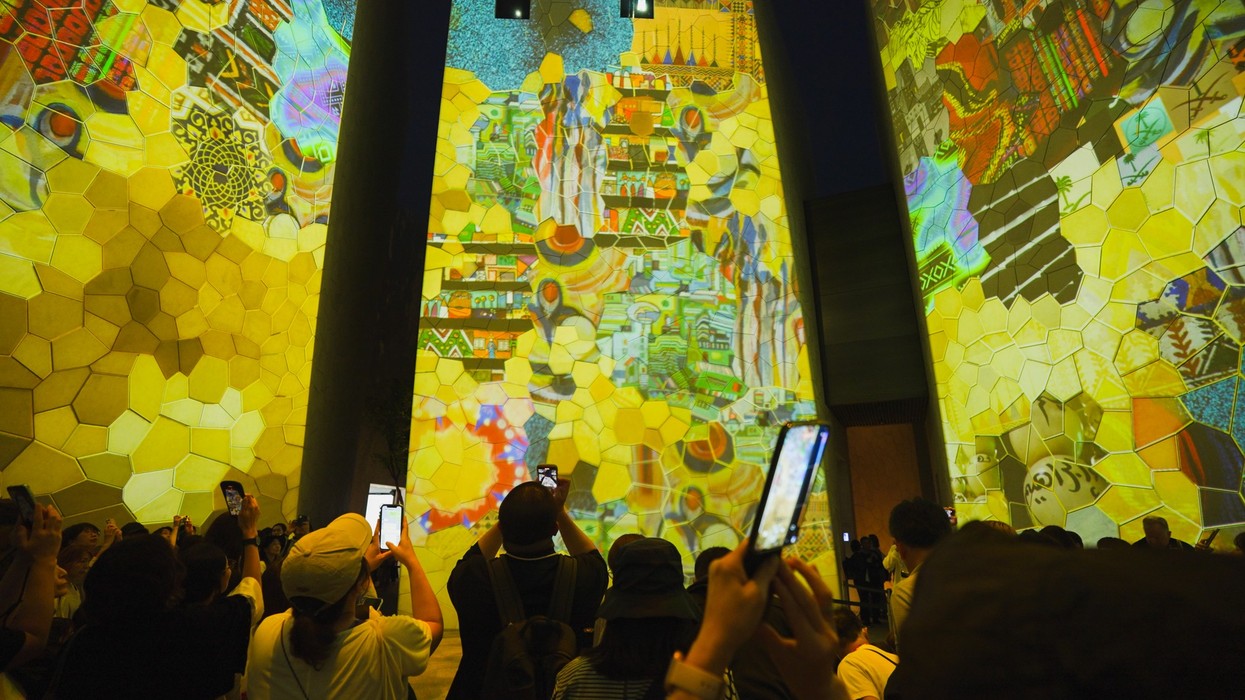 People capturing colorful digital art projections on large walls with phones.