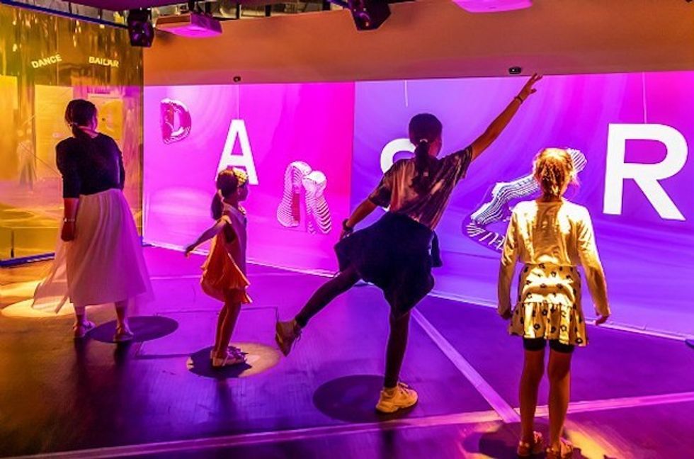 People dancing in front of a colorful wall with large letters.