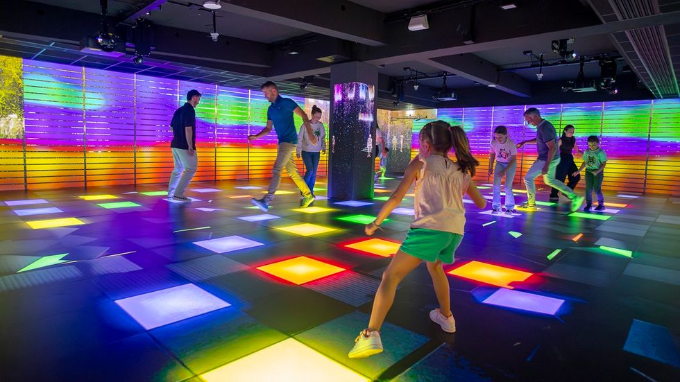 People dancing on a colorful, illuminated floor in a vibrant, modern room, at Pulse! The Electric Odyssey