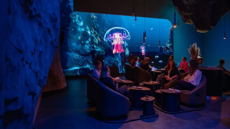 People eat and drink during Eatrenalin with a large screen featuring glowing jellyfish.