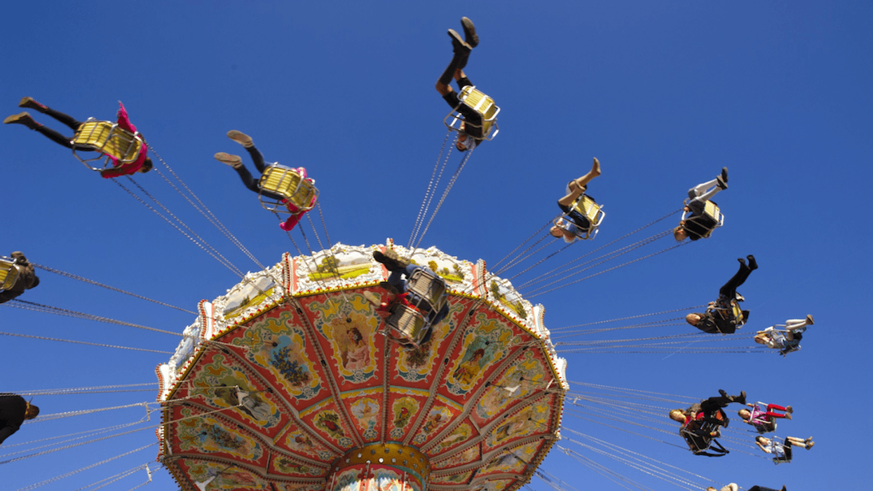 People enjoy a colorful swing ride against a clear blue sky.