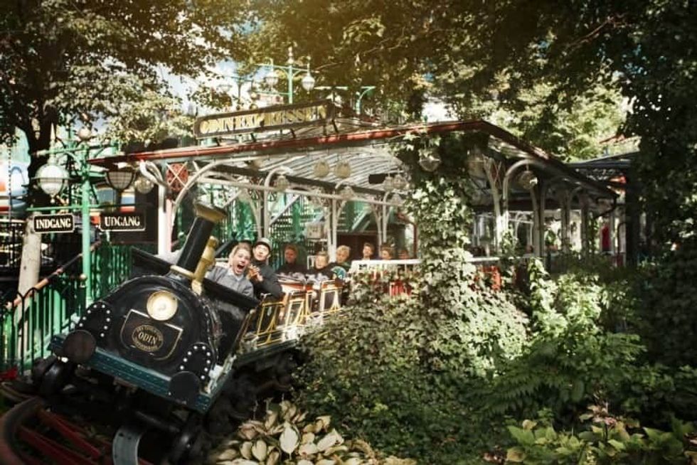 People enjoy a vintage train ride surrounded by lush greenery at Tivoli Gardens