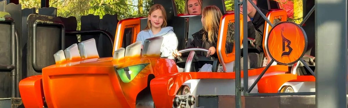 People enjoy an amusement park ride in an orange monster-themed vehicle.