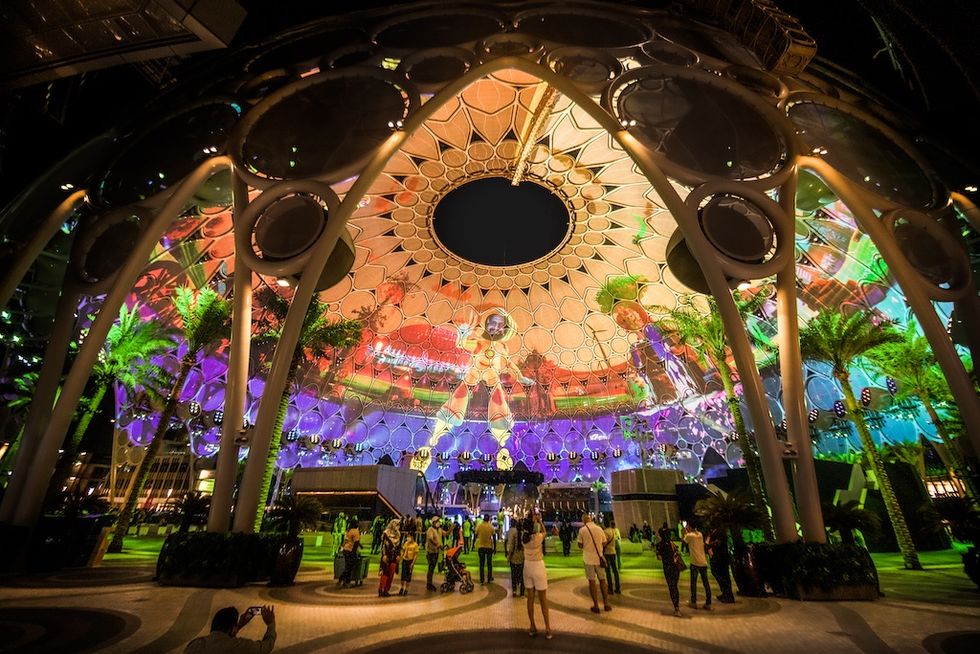 People enjoy colorful light displays under a large, circular architectural canopy.