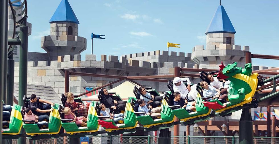 People enjoying a dragon-themed roller coaster ride in front of a castle backdrop.