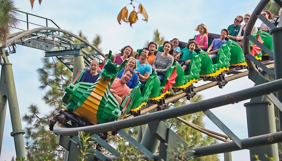 People enjoying a dragon-themed roller coaster ride, surrounded by trees.