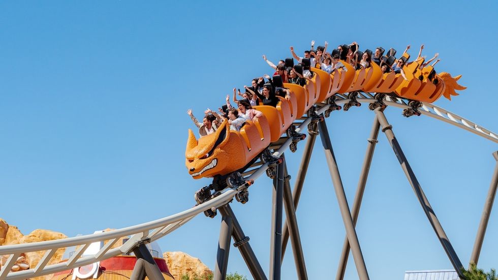 People enjoying a dragon-themed roller coaster under a clear blue sky.