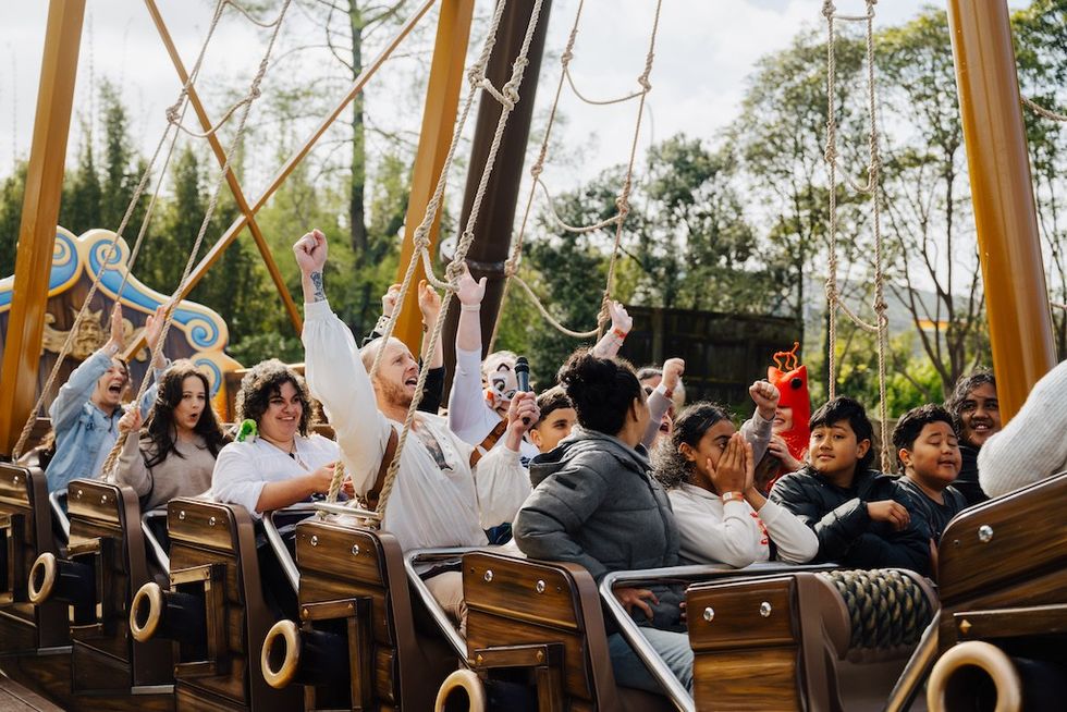 People enjoying a pirate ship ride at an amusement park, arms raised with various expressions.
