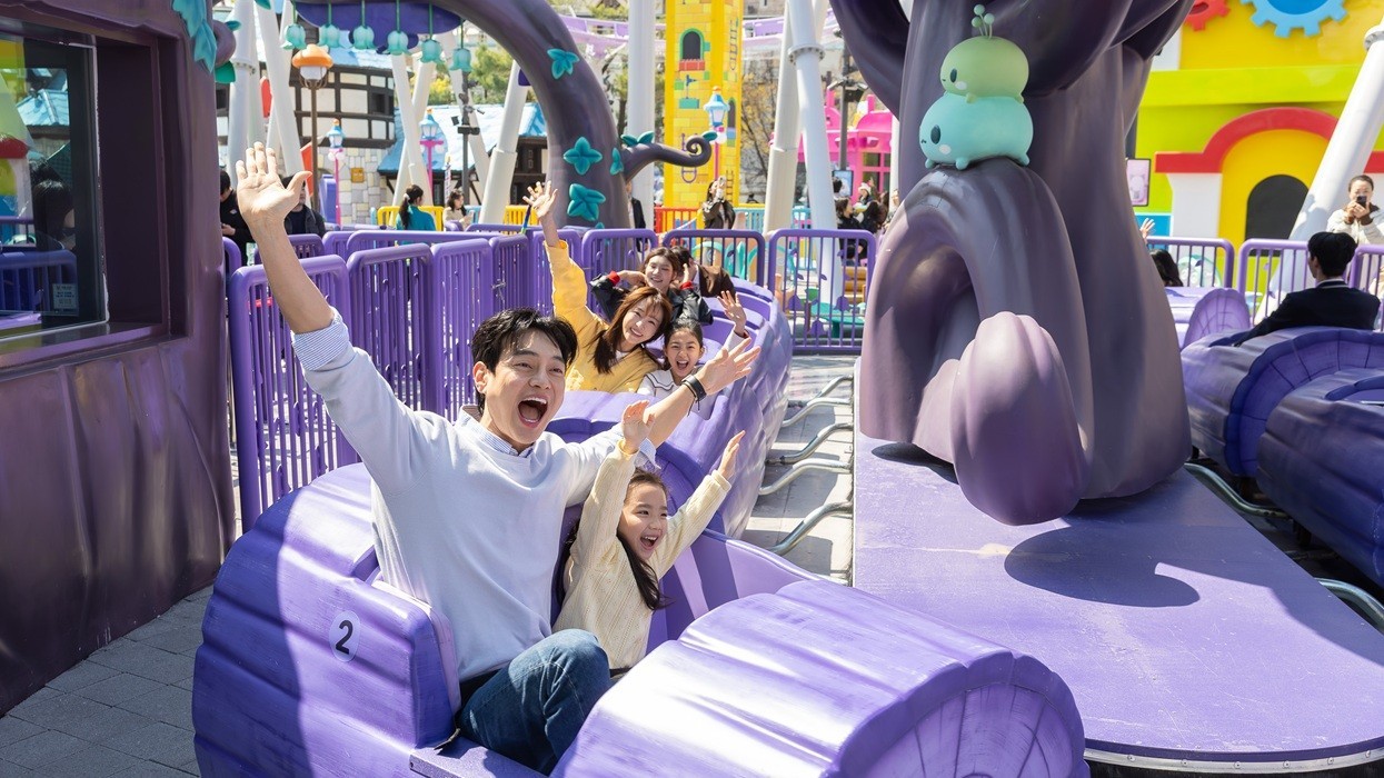 People enjoying a ride in purple roller coaster cars at an amusement park.