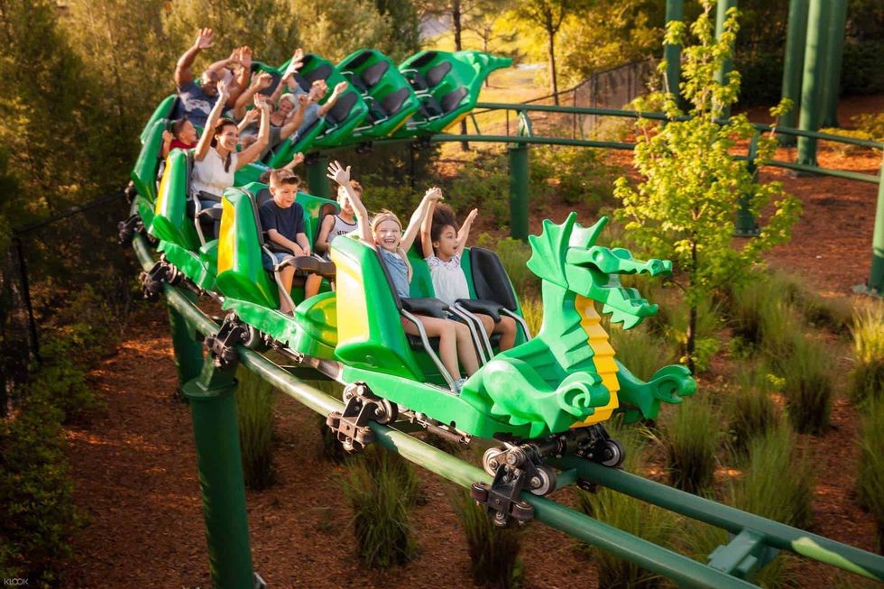 People enjoying a ride on a green dragon-themed roller coaster amid greenery.