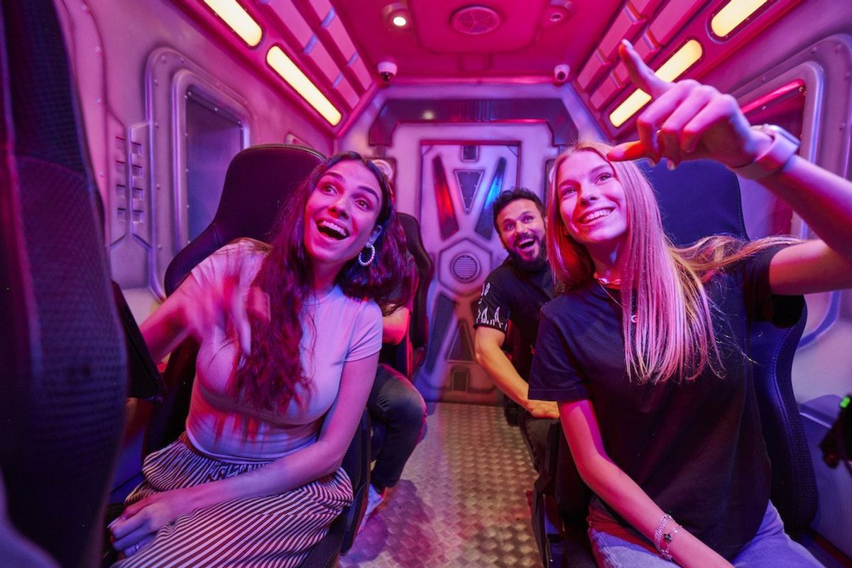 People enjoying a ride with vibrant pink lighting, pointing and smiling excitedly.