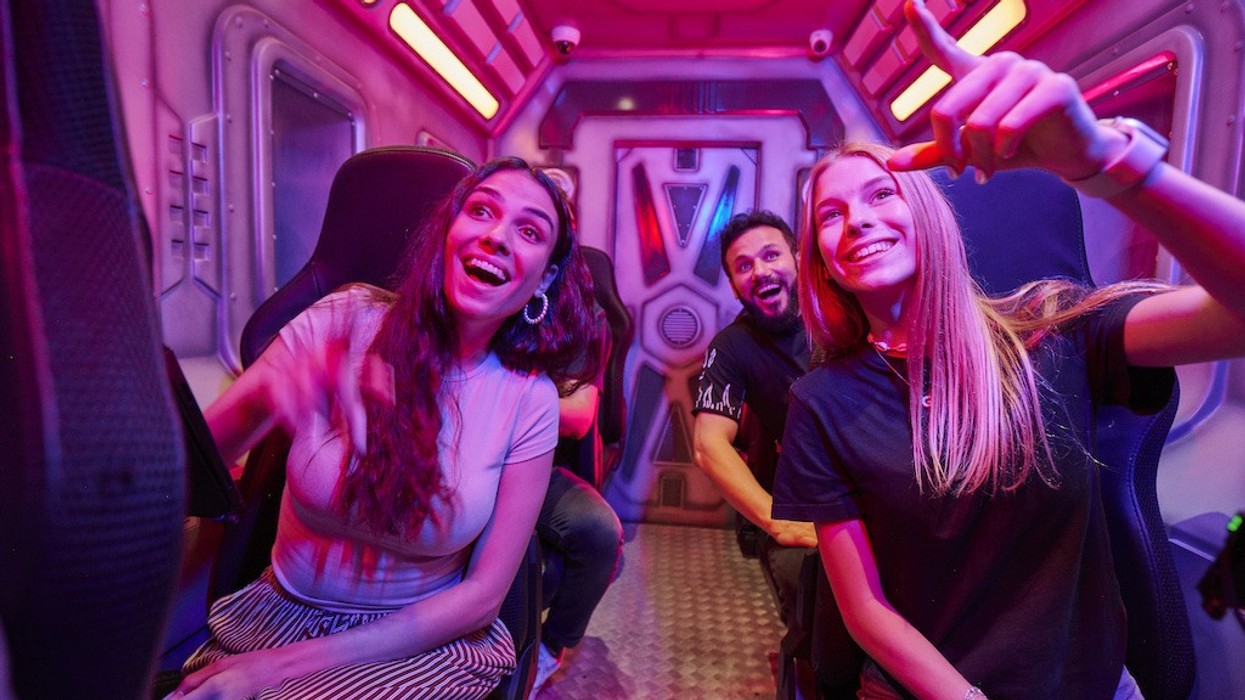 People enjoying a ride with vibrant pink lighting, pointing and smiling excitedly.
