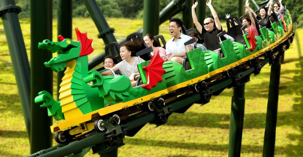 People enjoying a roller coaster ride on a dragon-themed car in a lush green park.