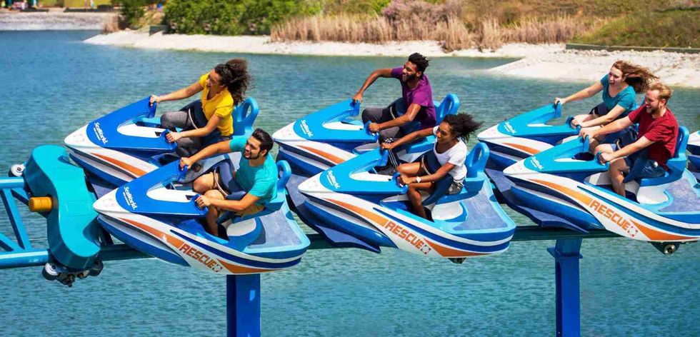 People enjoying a roller coaster ride on water-themed jet ski cars over a body of water.