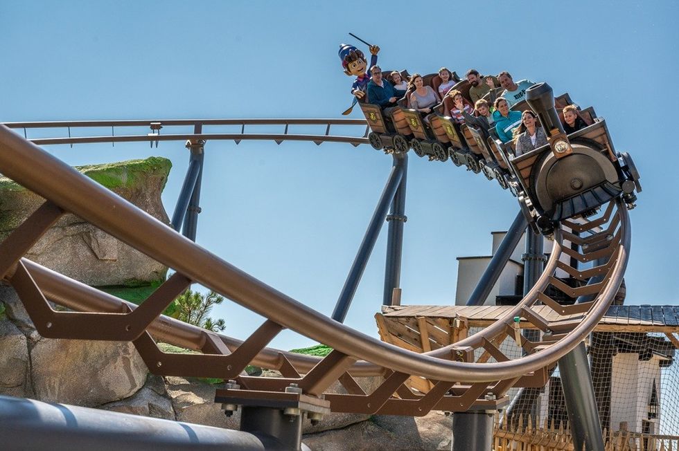 People enjoying a roller coaster ride shaped like a train on a sunny day.