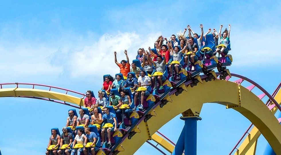 People enjoying a roller coaster ride with arms raised under a clear blue sky at Six Flags Great Adventure