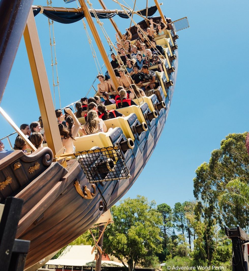 People enjoying a swinging pirate ship ride under a clear blue sky.