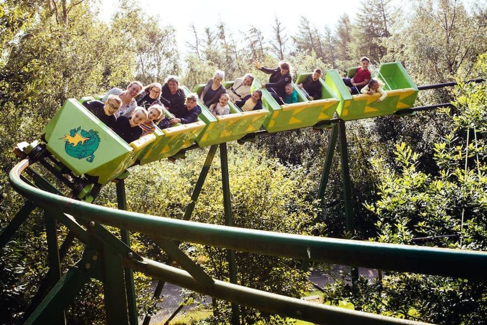 People enjoying a The Green Dragon roller coaster ride through a lush, wooded area.