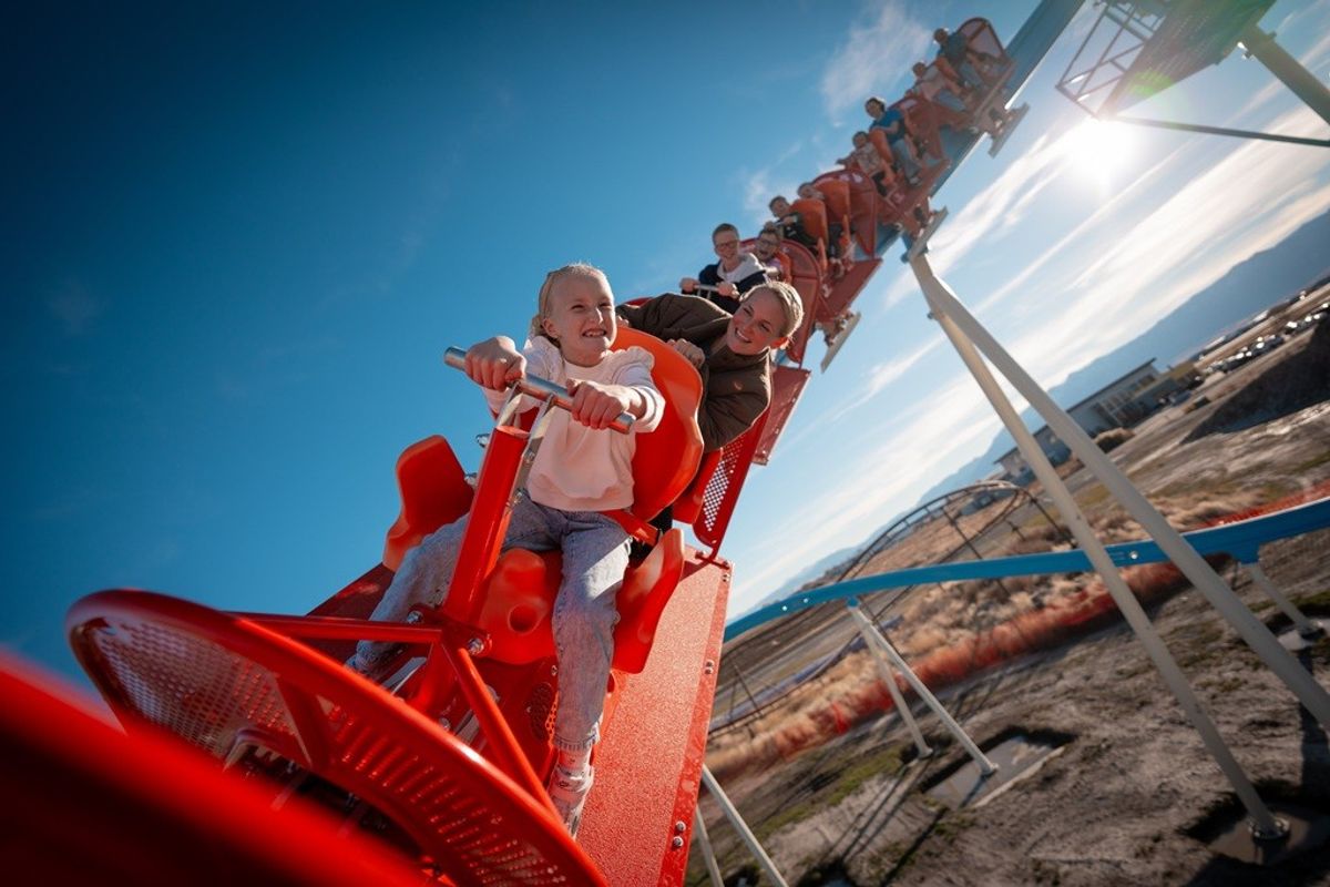 People enjoying a thrilling red roller coaster ride under a clear blue sky.