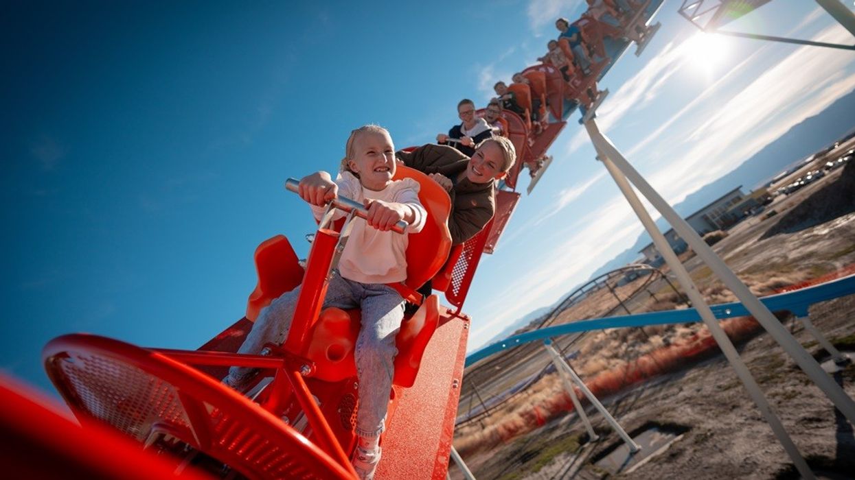 People enjoying a thrilling red roller coaster ride under a clear blue sky.
