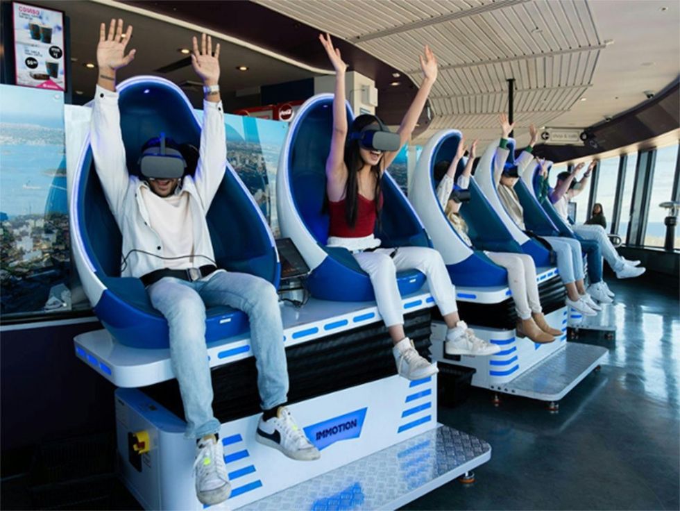 People enjoying a VR ride in individual pod chairs with arms raised, experiencing a simulation.