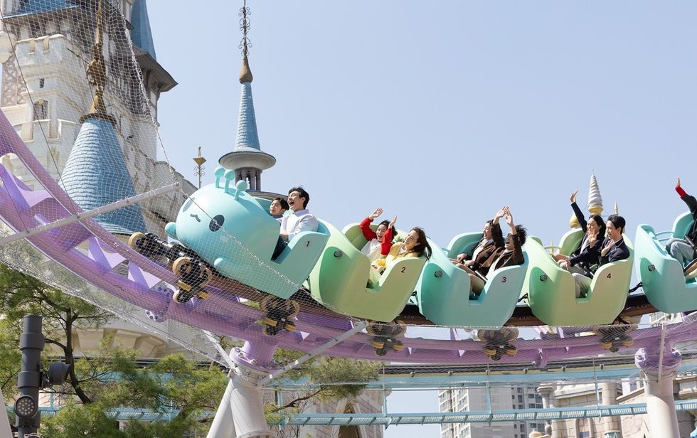 People enjoying a whimsical roller coaster by a fairytale castle.