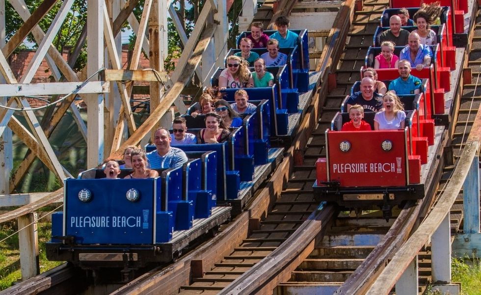 People enjoying grand National - a wooden roller coaster ride with blue and red cars at Pleasure Beach.