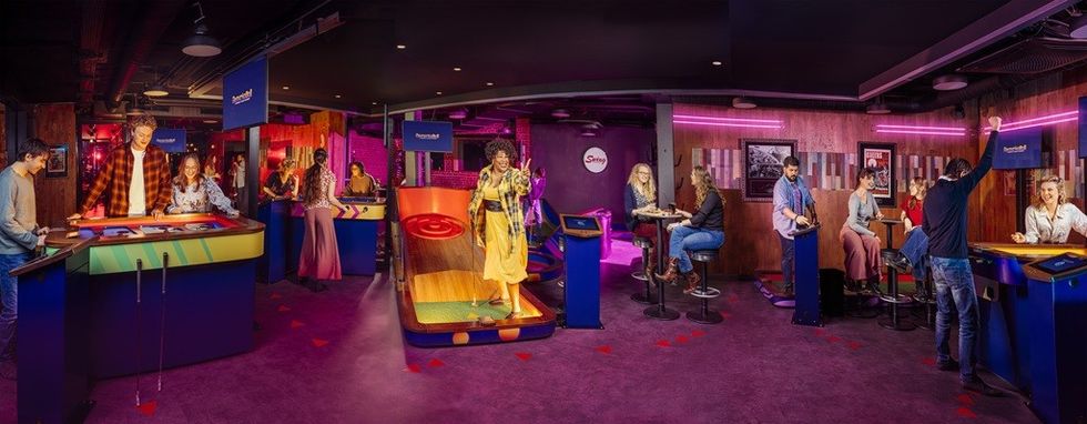 People enjoying various interactive games in a dimly lit, neon-accented gaming lounge.