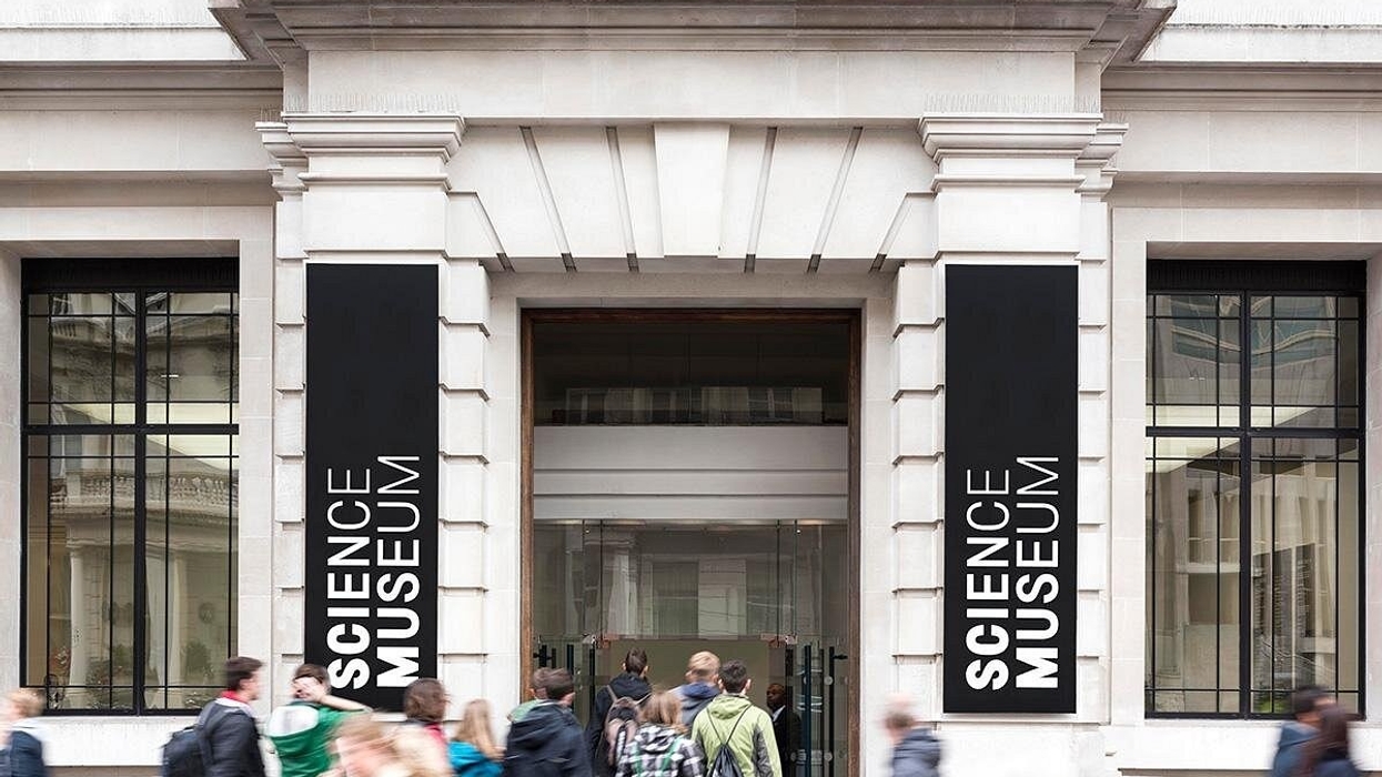 People entering the Science Museum through its main entrance with large signs.