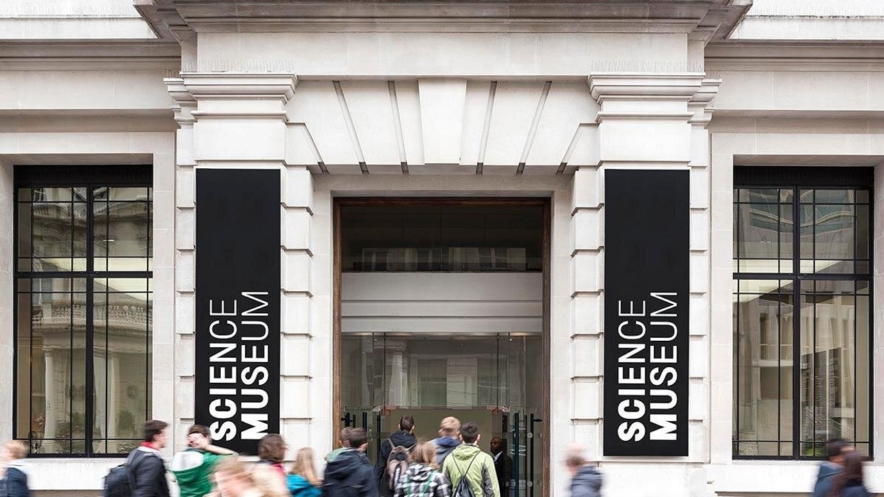 People entering the Science Museum through its main entrance with large signs.