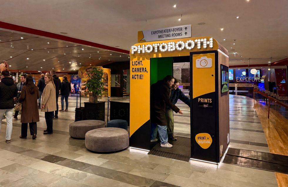 People exiting a brightly lit photobooth in a modern, spacious indoor venue.