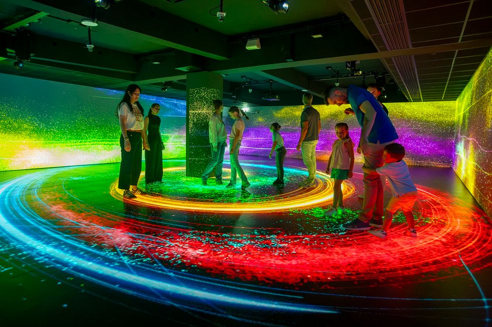 People explore an immersive, colorful digital art installation with swirling light patterns at Pulse! The Electric Odyssey