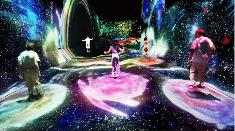 People exploring a colorful, immersive digital art space with cosmic projections at teamLab Borderless