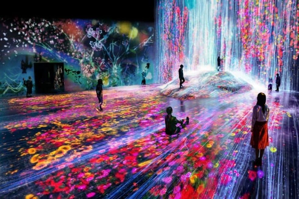 People exploring a vibrant, colorful digital art installation with cascading lights, teamLab
