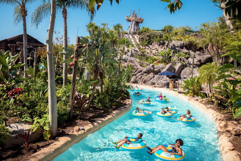 People float on a lazy river in a lush, tropical water park with a ship mast in background at Typhoon Lagoon