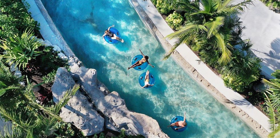 People floating on inner tubes in a scenic, tropical lazy river surrounded by lush greenery.