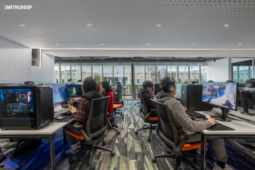 People gaming on computers in a modern eSports facility with large windows.