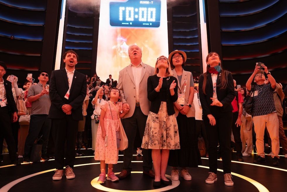 People gather around for the launch at USA Pavilion, Expo 2025,, gazing upwards in anticipation.