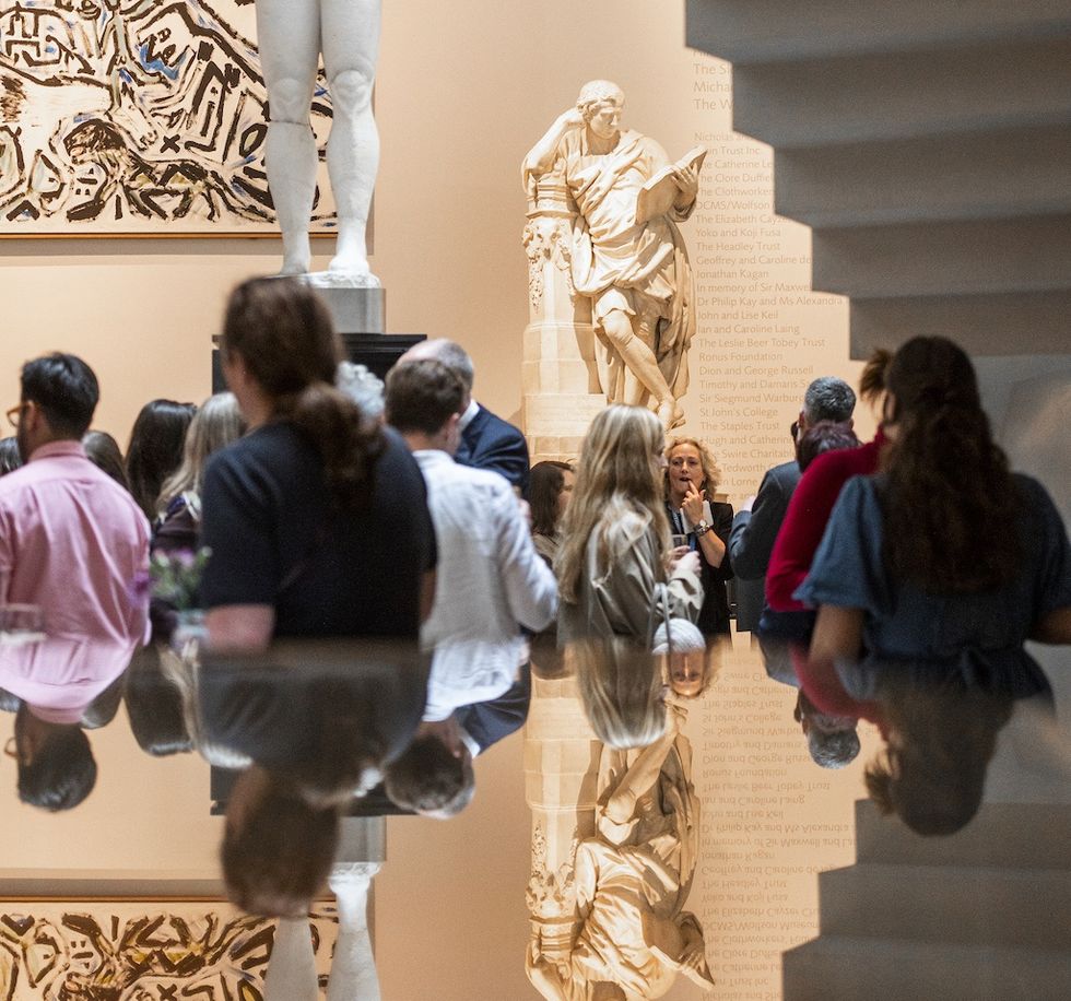 People gather in an art museum near classical sculptures and abstract paintings.