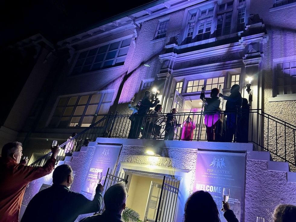 People gather outside a lit-up building at night, raising glasses in celebration.