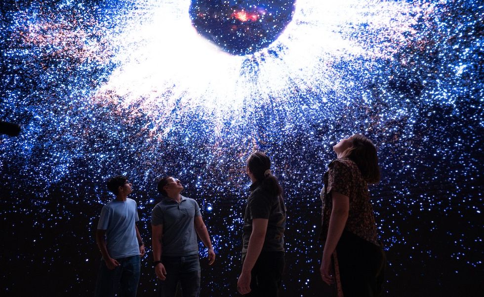 People gazing at a cosmic projection with a bright central light and surrounding stars.